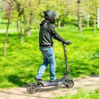Man riding Ausom DT2 Pro electric scooter on a green trail wearing helmet and casual clothes